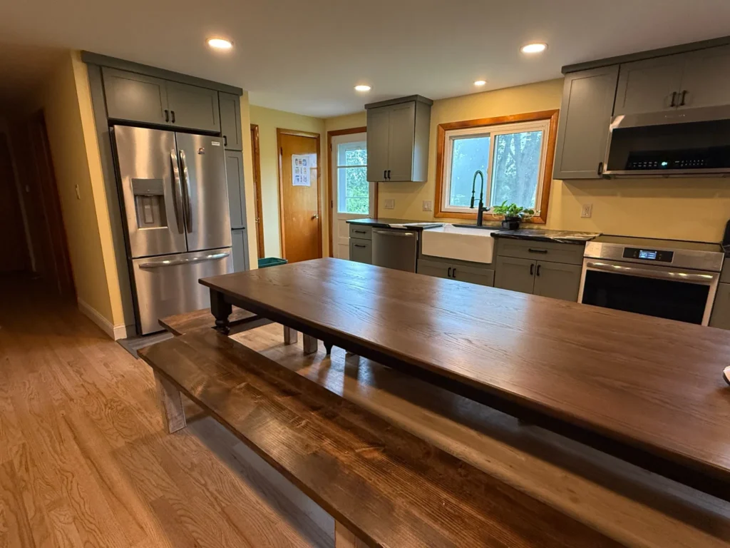 Remodeled kitchen with gray cabinets, French-door refrigerator and a long wooden dining table with a bench