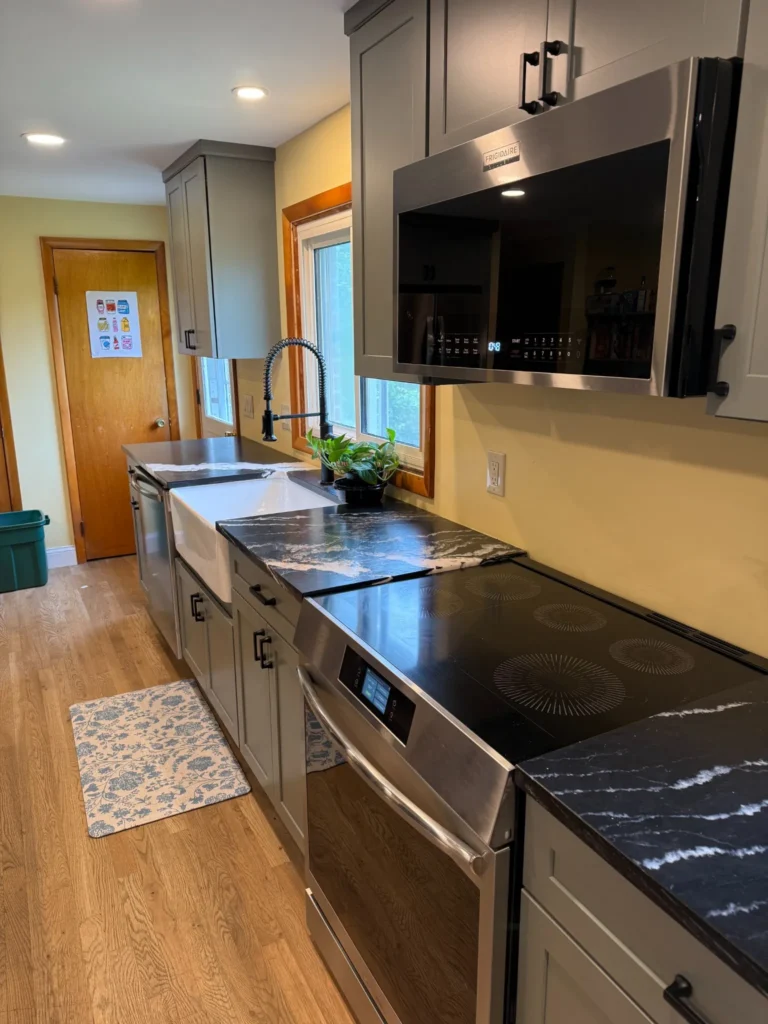 Gray cabinets with black-and-white veined countertops, an electric range, stainless microwave and a farmhouse sink