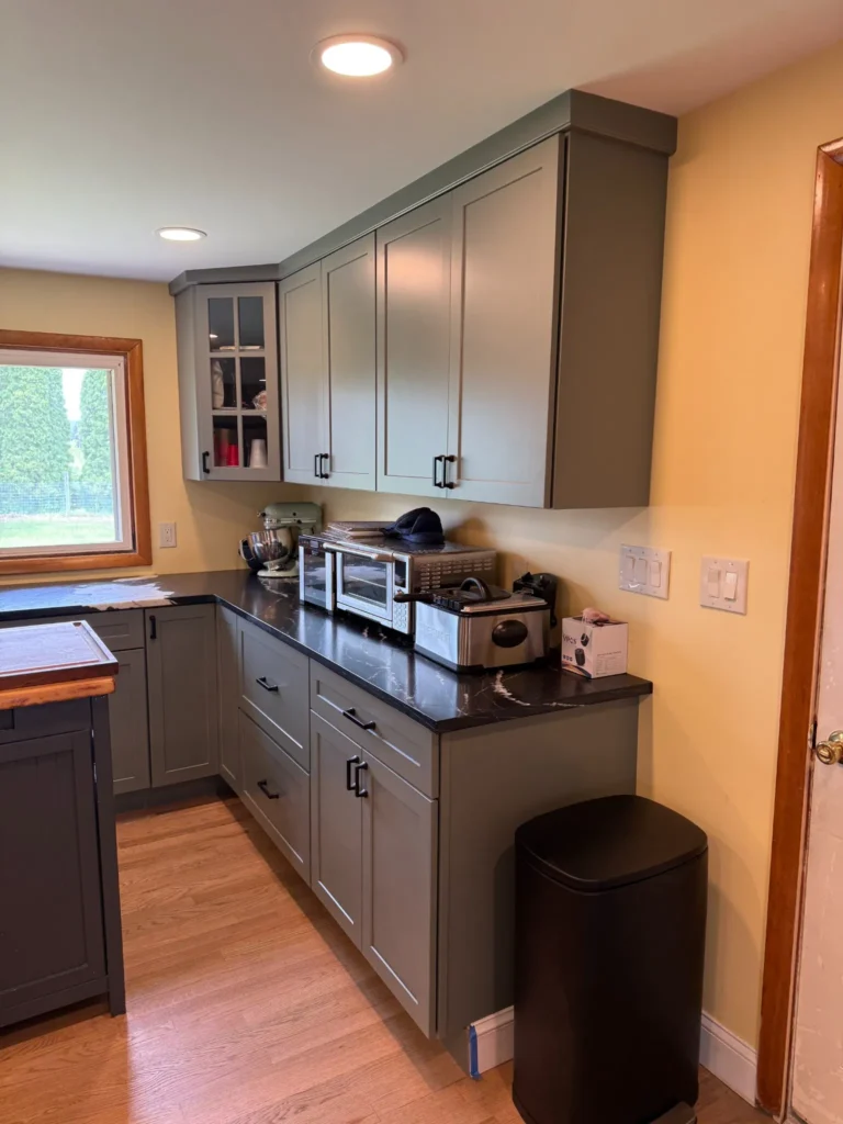 Corner of the new kitchen with gray Shaker cabinets, a glass-front upper cabinet, black countertops and recessed lighting