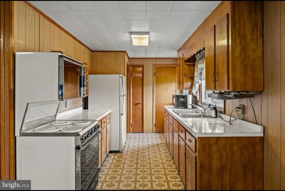Narrow wood-cabinet galley kitchen with white appliances, white countertops and a yellow patterned floor